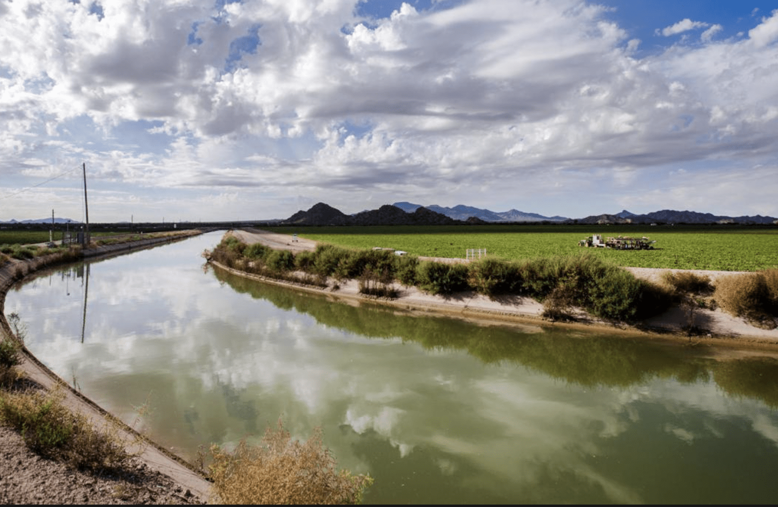 Irrigation canal reflecting clouds beside farmland