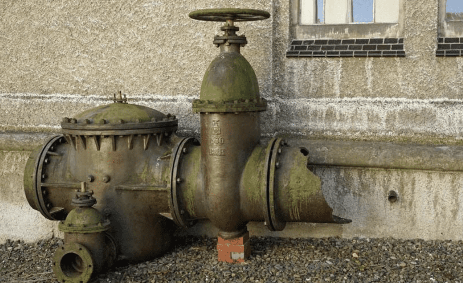 Aged green metal water valve assembly by wall