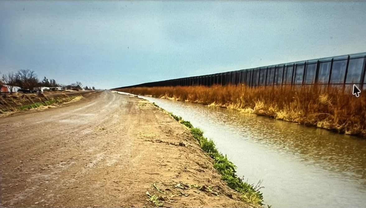 Dirt road alongside canal with long fence